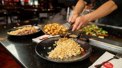 Chef scoops fried rice from a grill onto a black plate at a teppanyaki table