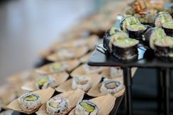 Assorted sushi rolls arranged on trays at a buffet, with black and beige serving dishes.