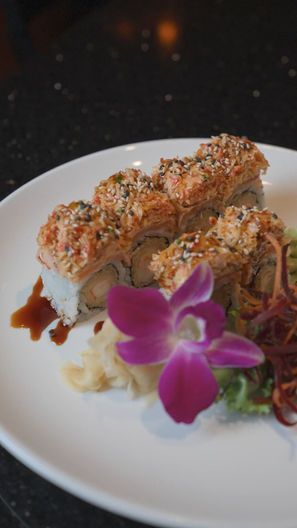 Sushi rolls on a white plate, garnished with herbs and a purple orchid flower.