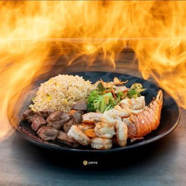 Plate of grilled meat, shrimp, salmon, rice, and vegetables surrounded by dramatic flames