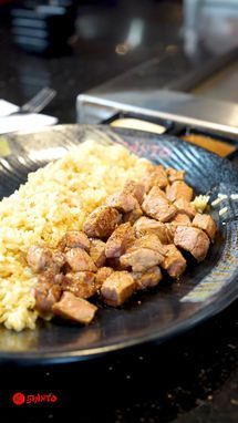 Black plate with diced grilled meat and yellow rice on a restaurant table.