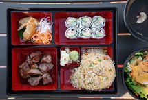 Sushi bento box with rolls, fried dumplings, meat, salad, and fried rice in red trays