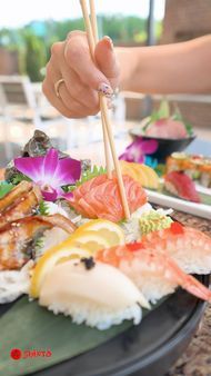 Hand using chopsticks to pick salmon sushi on a black plate with purple flower garnish