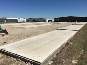 A series of rectangular concrete pads set into a gravel lot, with industrial buildings in the background.