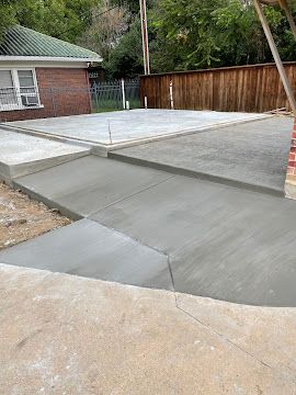 Freshly poured concrete patio and walkway transition extending from a brick house toward a wooden fence.