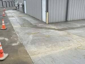 A gray concrete alleyway outside a metal storage building with orange traffic cones lining the edge.