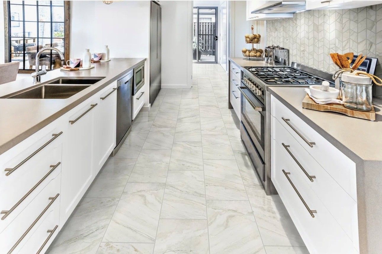 Bright modern kitchen with white cabinets, marble island, stainless appliances, and a long central walkway