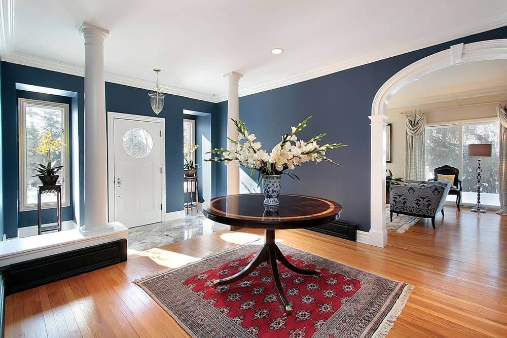 Bright foyer with blue walls, white columns, a round table with flowers, and hardwood floors leading to a sitting room.