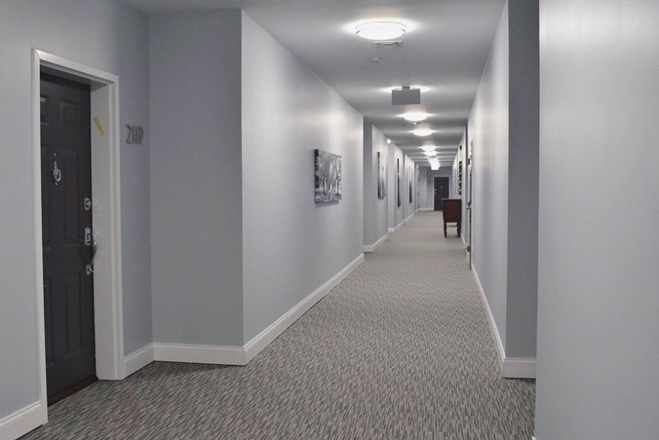 Long office hallway with gray walls, carpeted floor, and ceiling lights stretching into the distance