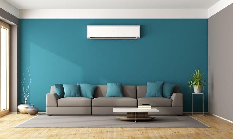 Modern living room with teal wall, gray sofa, wall AC, and small white coffee table