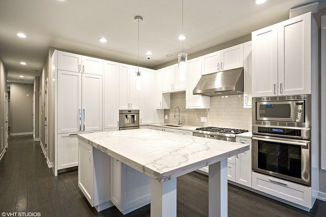 A kitchen with white cabinets , stainless steel appliances , and a large island.
