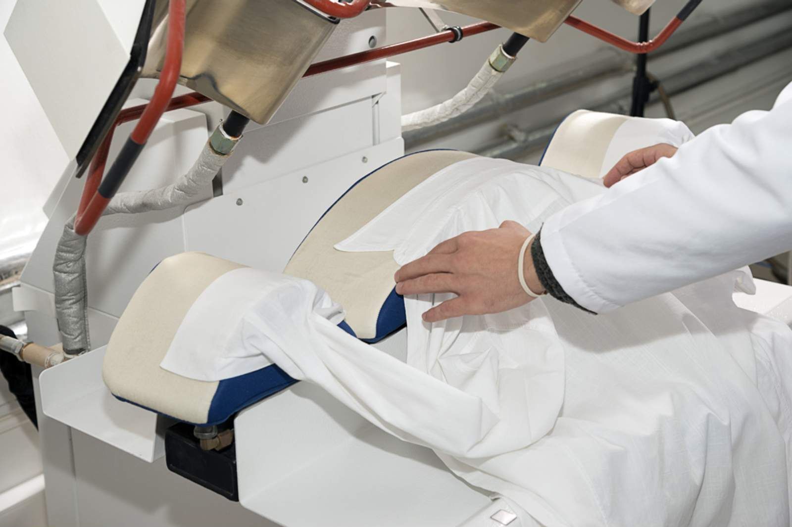 A Person Is Ironing A White Shirt On A Machine — Macquarie Dry Cleaners In Dubbo, NSW