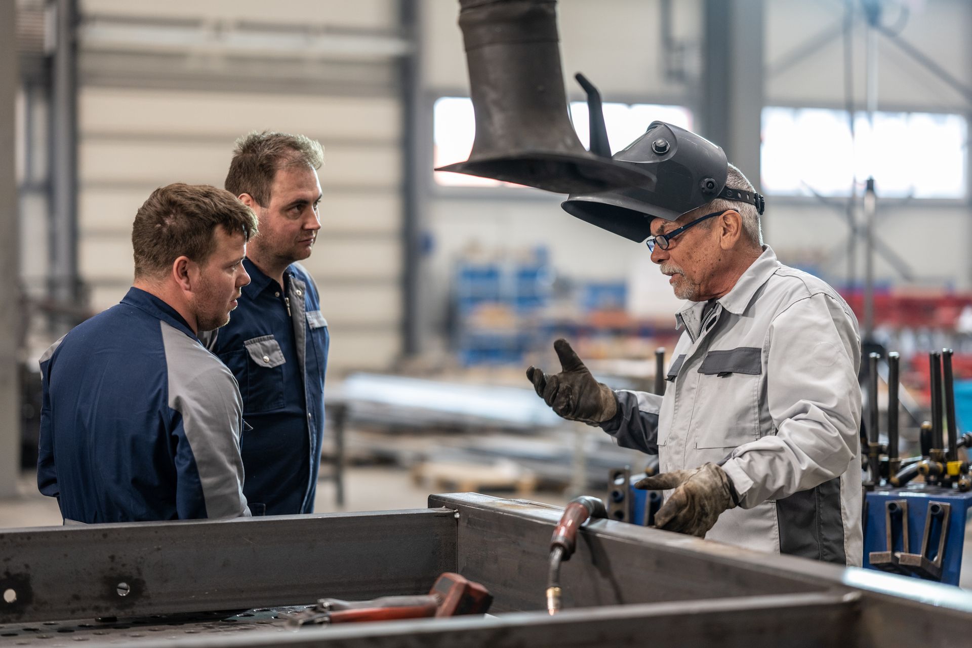 manufacturing workers conversing with a man welding a metal frame