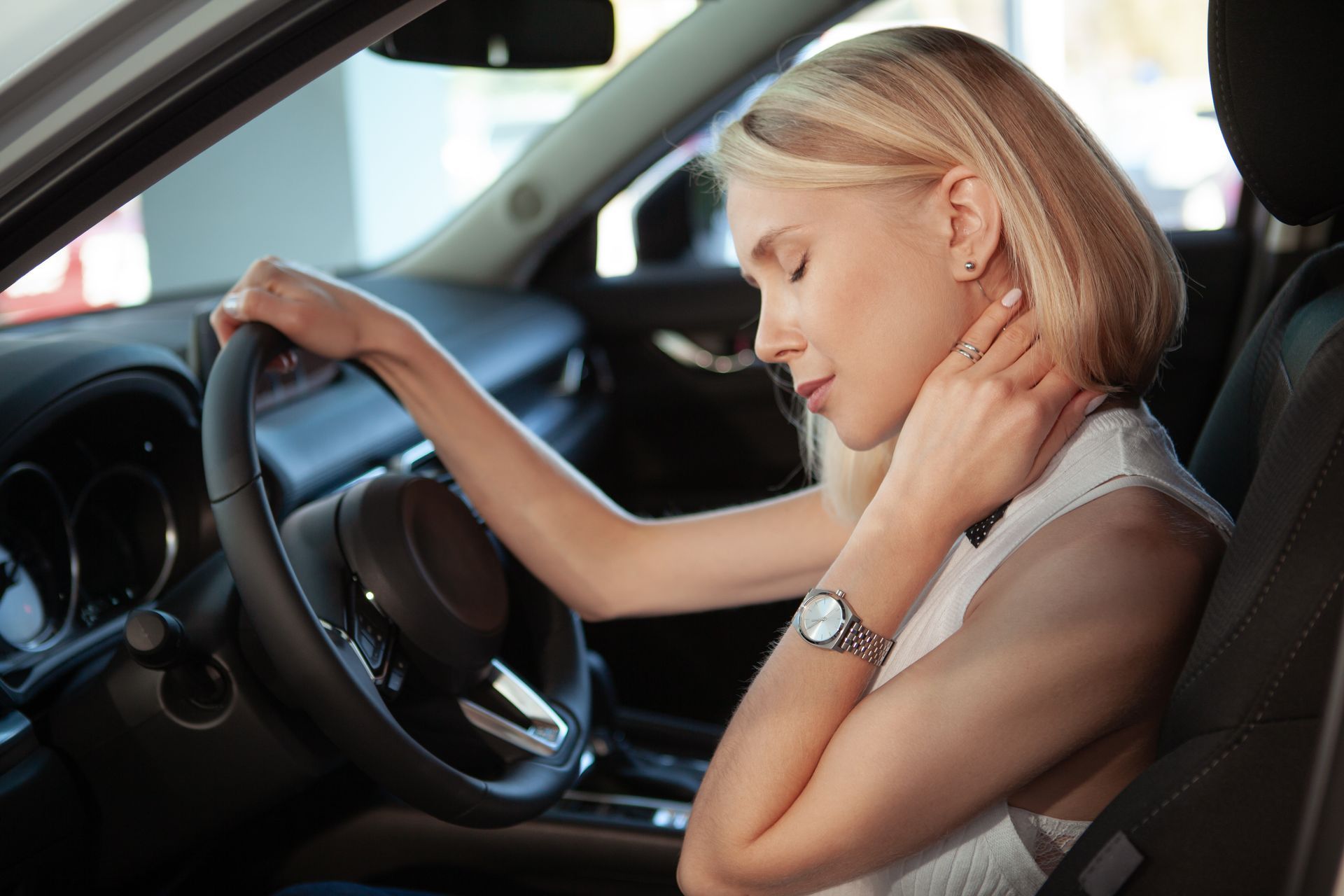 A woman is sitting in a car with her head on the steering wheel.