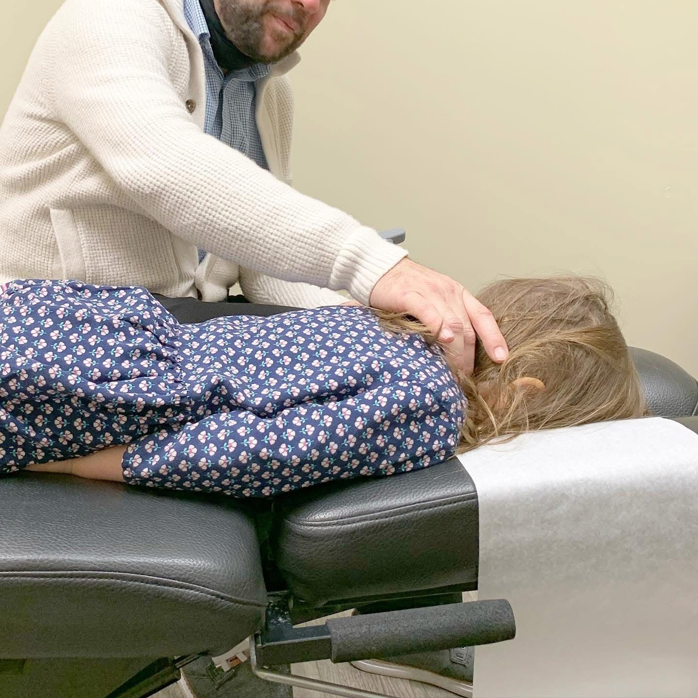 A man is adjusting a child 's back on a table.