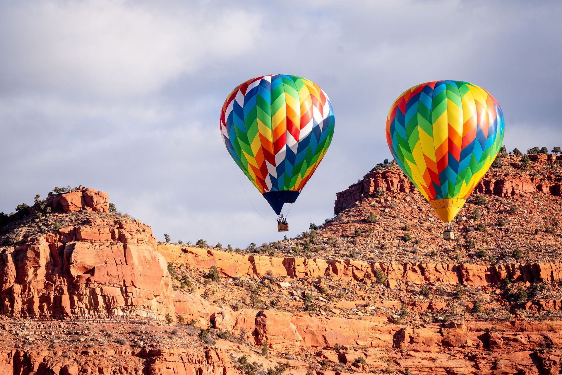 Two rainbow hot air balloons floating above a rocky desert landscape at sunrise
