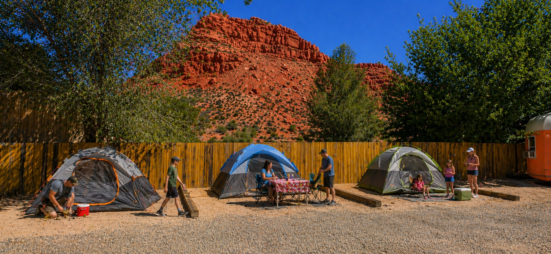 Camping tent under trees in a sunlit desert landscape with red rock cliffs in the background