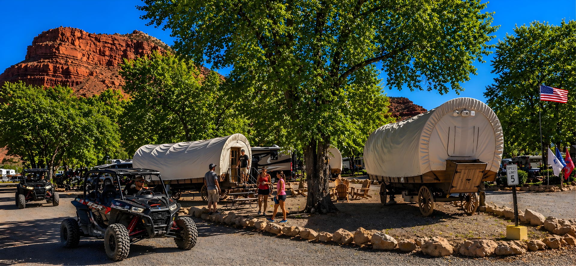 Covered wagon on a dirt path in a desert landscape with red cliffs and trees at sunset