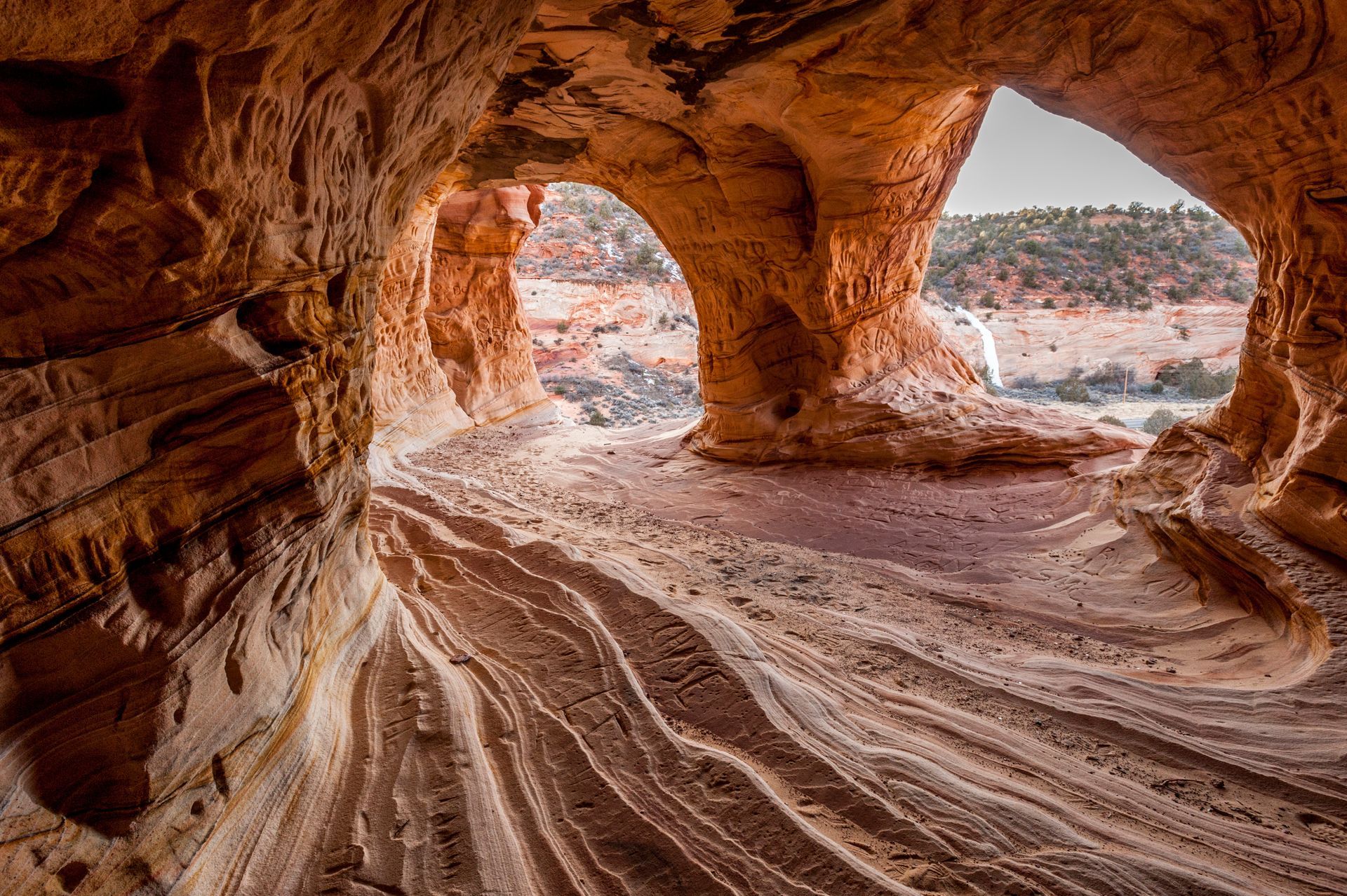 Rocky cave with striped sandstone floor and arched openings overlooking a desert landscape