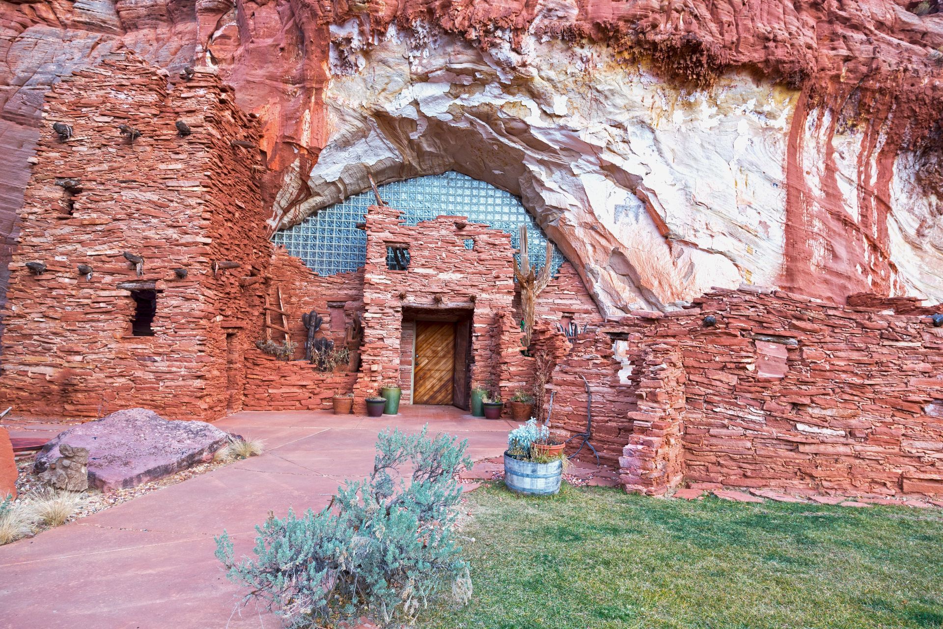 Ancient red rock ruins built into a sandstone cliff with an arched opening and desert path.