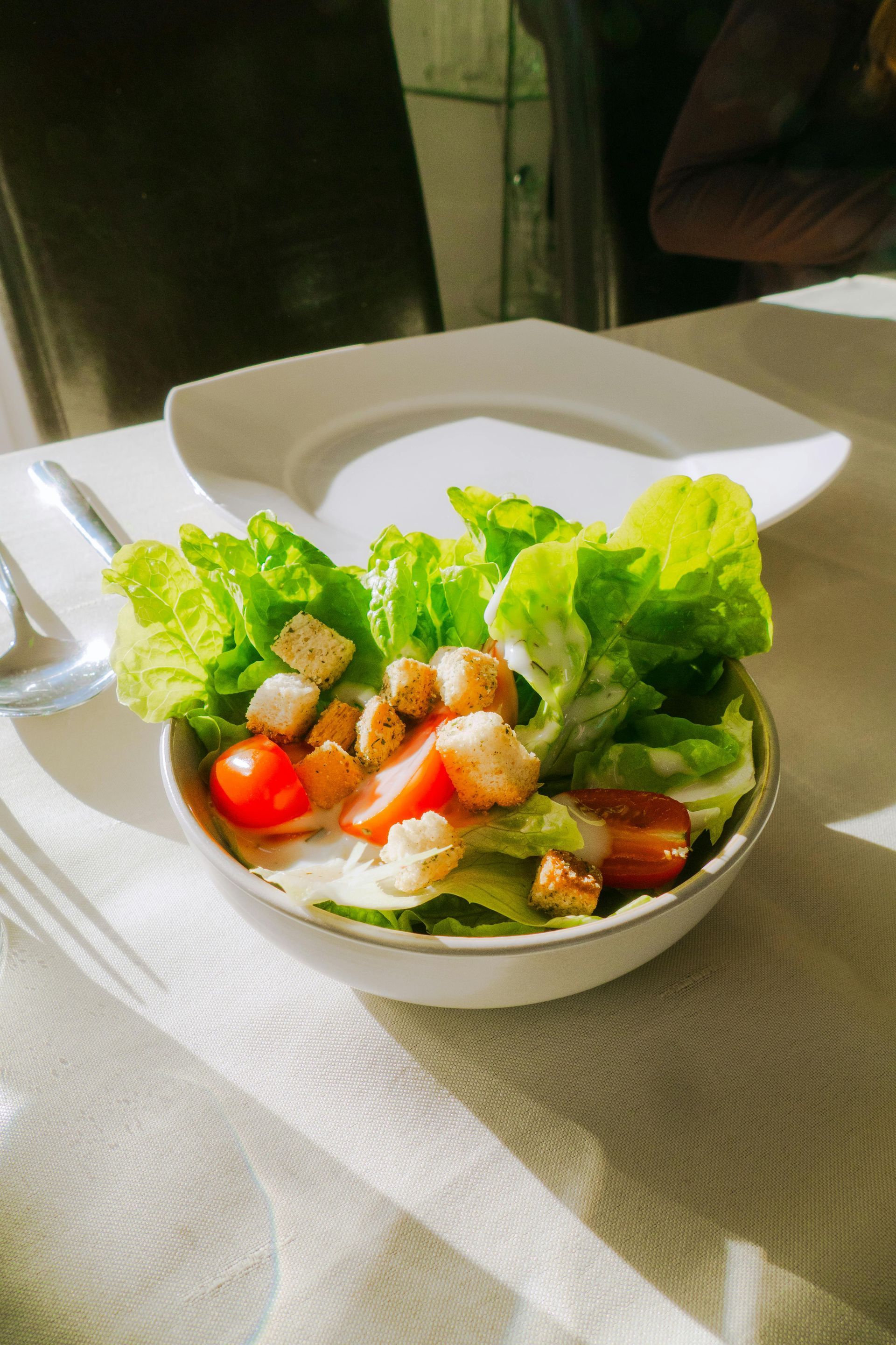 Fresh salad in a white bowl with lettuce, cherry tomatoes, and croutons on a table