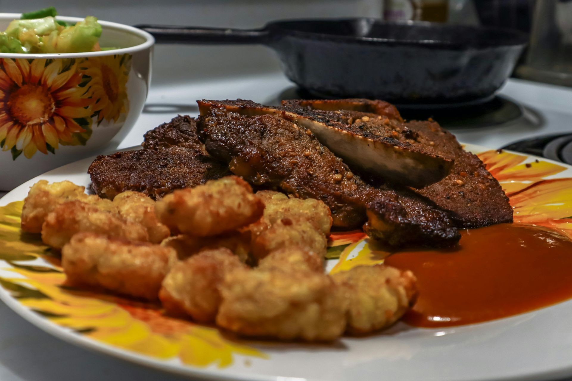 Plate of grilled meat and fried pieces with red sauce beside a small bowl of salad
