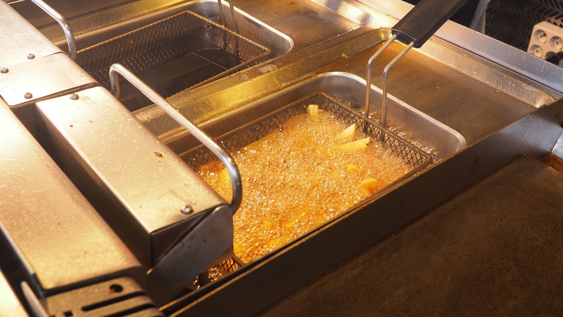 French fries cooking in bubbling hot oil commercial deep fryer restaurant kitchen equipment.