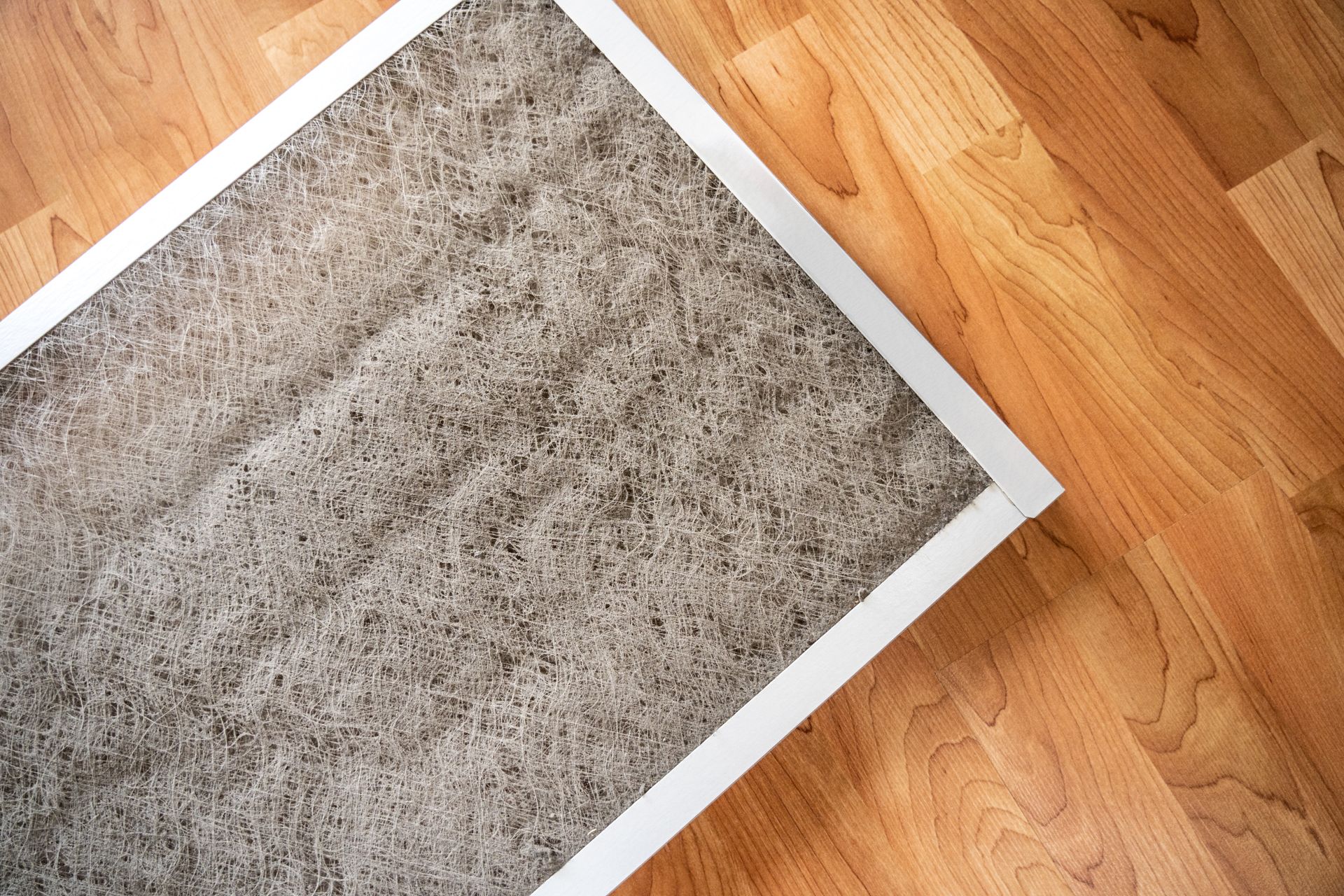 Dirty home air filter covered in dust and lint lying on a wooden floor.