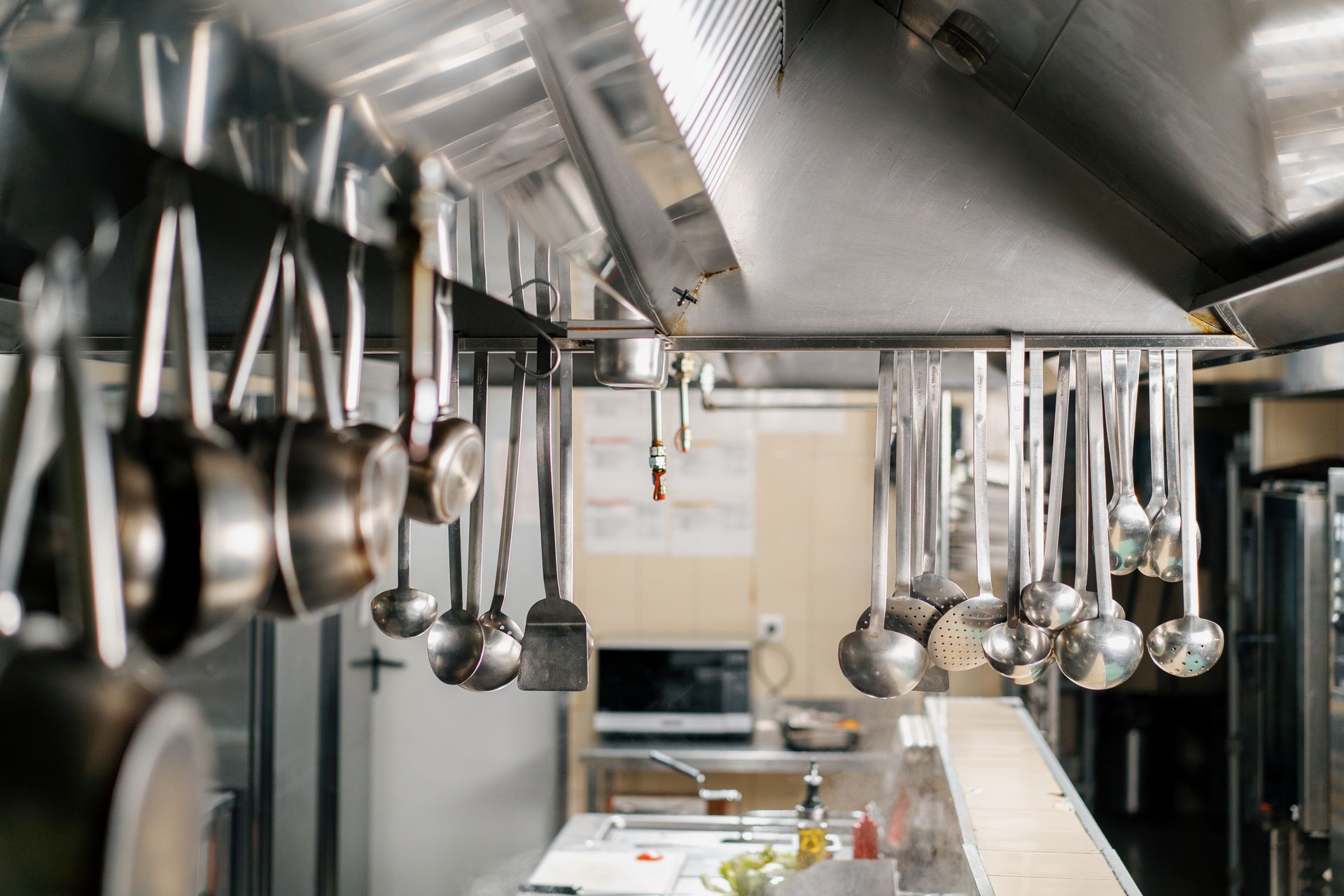 A professional kitchen hood has dishes and ladles hanging above cooking equipment.