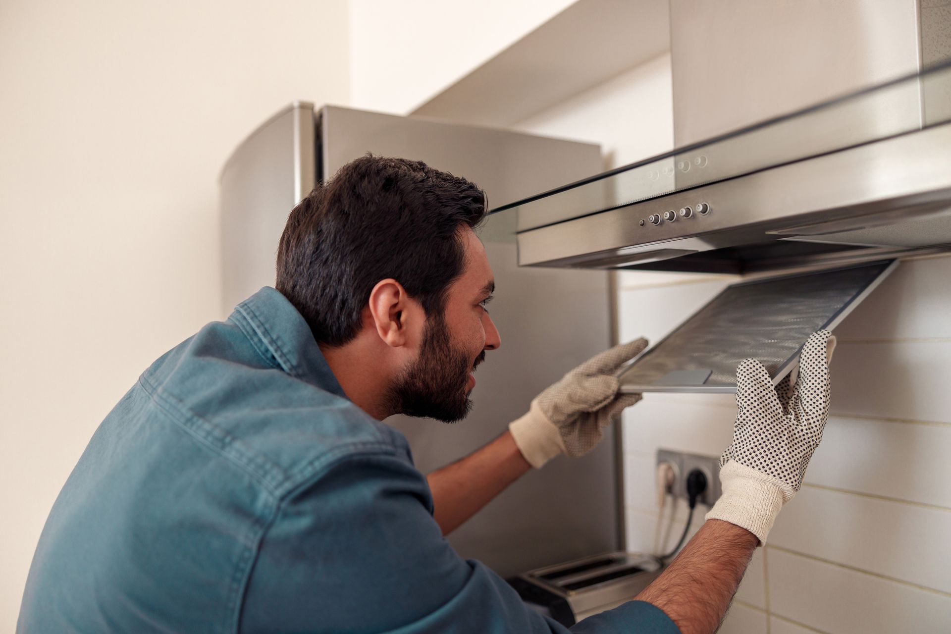 Technician performing commercial kitchen fan repair while inspecting metal range hood filter.