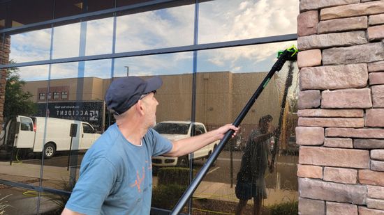 Person using a squeegee to clean soapy foam from a window against a blue sky