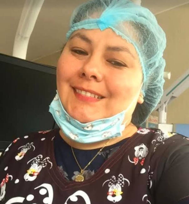 Persona sonriente con gorro azul para el cabello y camisa negra estampada, en un espacio interior.