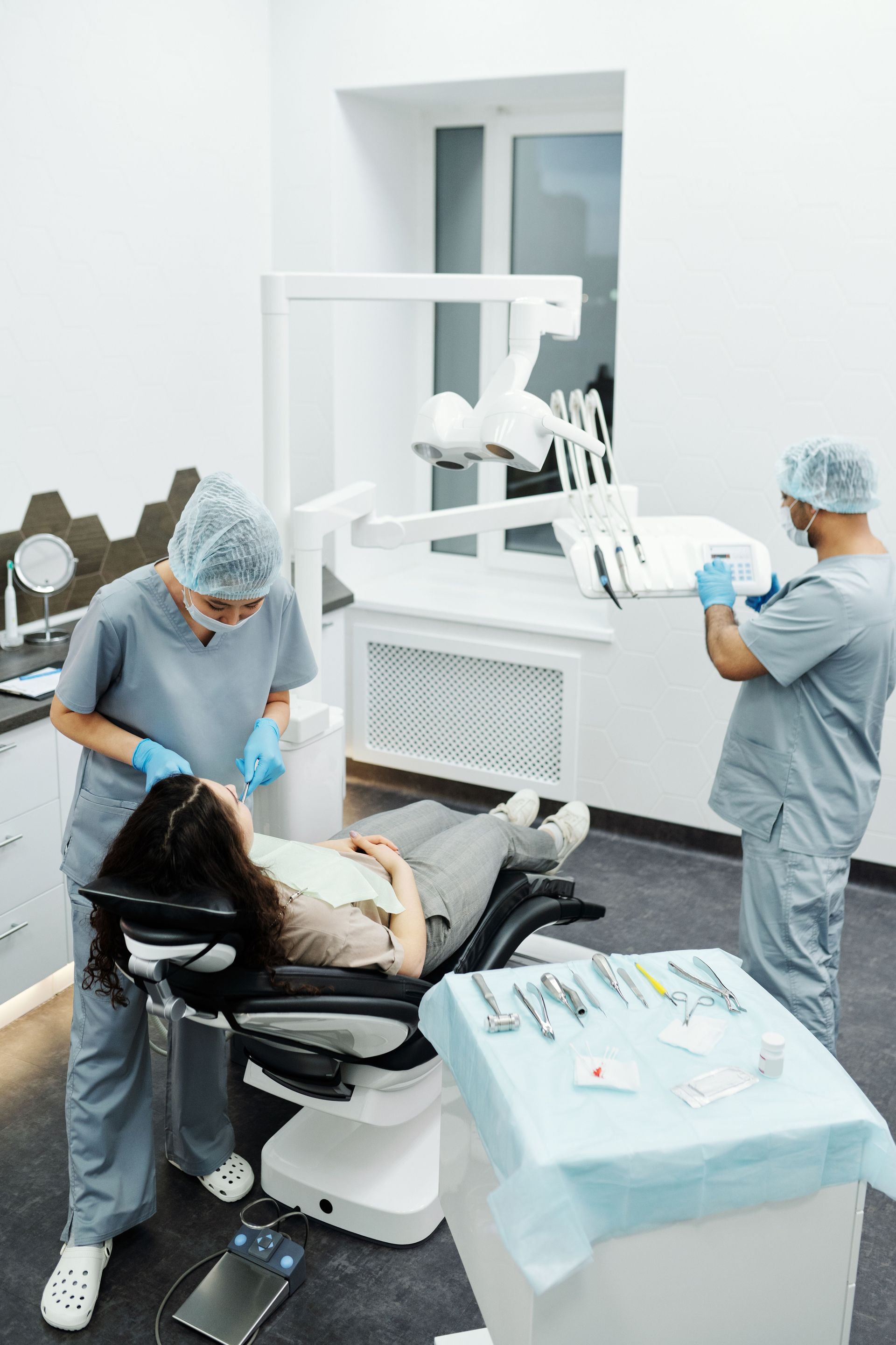 Dentista y asistente atendiendo a un paciente en una clínica dental luminosa, con un monitor instalado y una bandeja de instrumentos