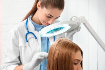 Un parrucchiere acconcia i capelli di una cliente sotto una lampada d'ingrandimento in un salone.