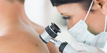 Medico che esamina la schiena di un paziente con un endoscopio portatile, indossando una mascherina