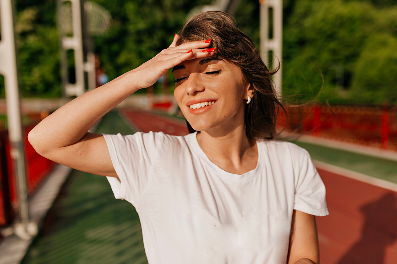 Una donna con una camicia bianca si ripara gli occhi dal sole su una pista di atletica rossa.