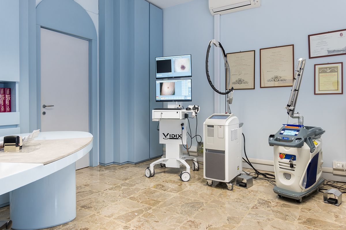 Moderna sala per trattamenti medici con apparecchiature laser ed estetiche, pareti blu e certificati incorniciati.