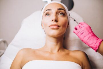 Una donna riceve un trattamento viso mentre una mano con un guanto rosa le applica un prodotto sulla fronte.