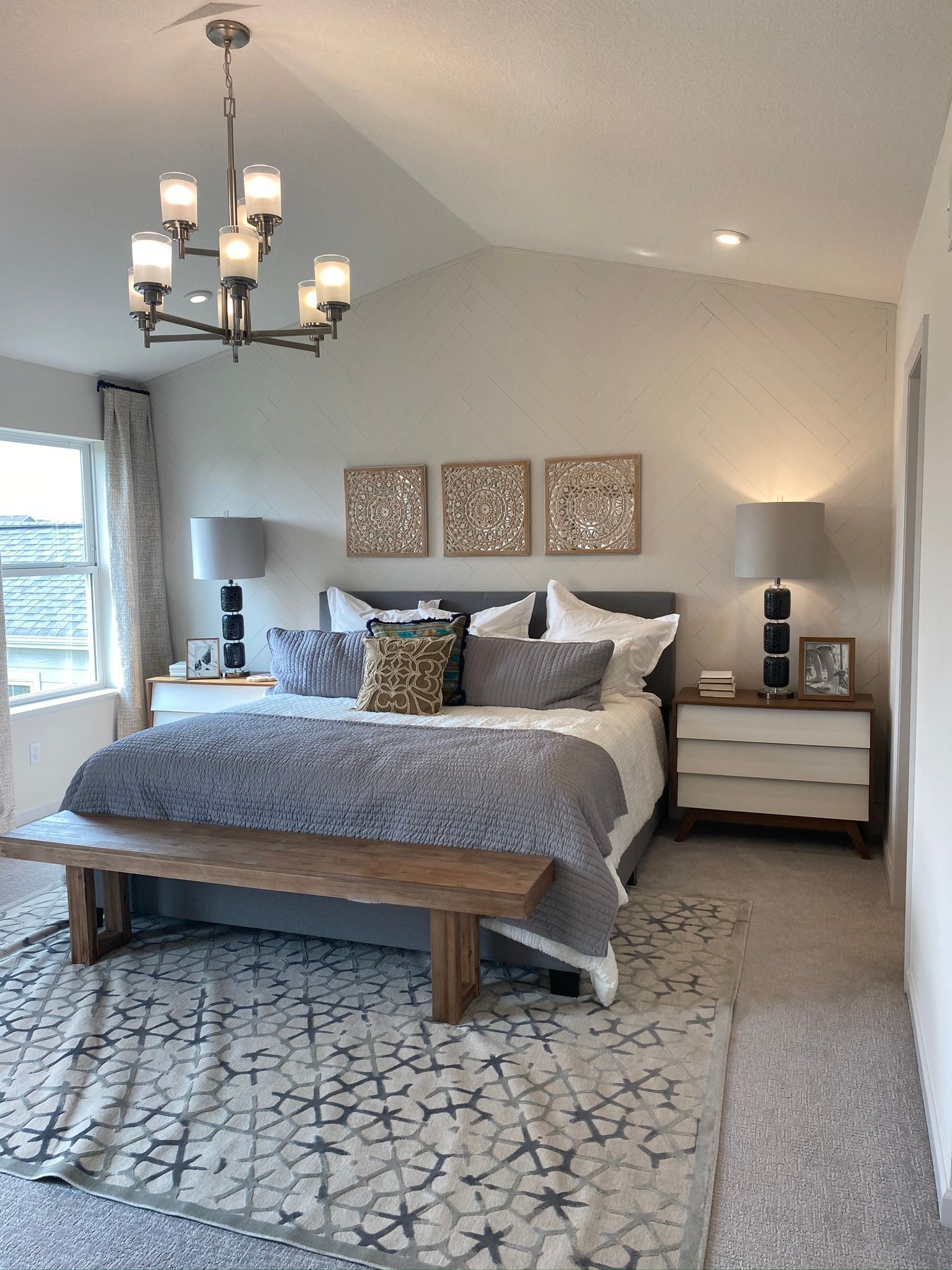 A bedroom with a bed , bench , nightstand , and chandelier.