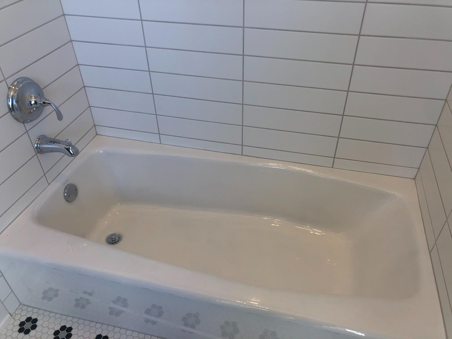 A bathtub in a bathroom with white tiles and a black and white tile floor.