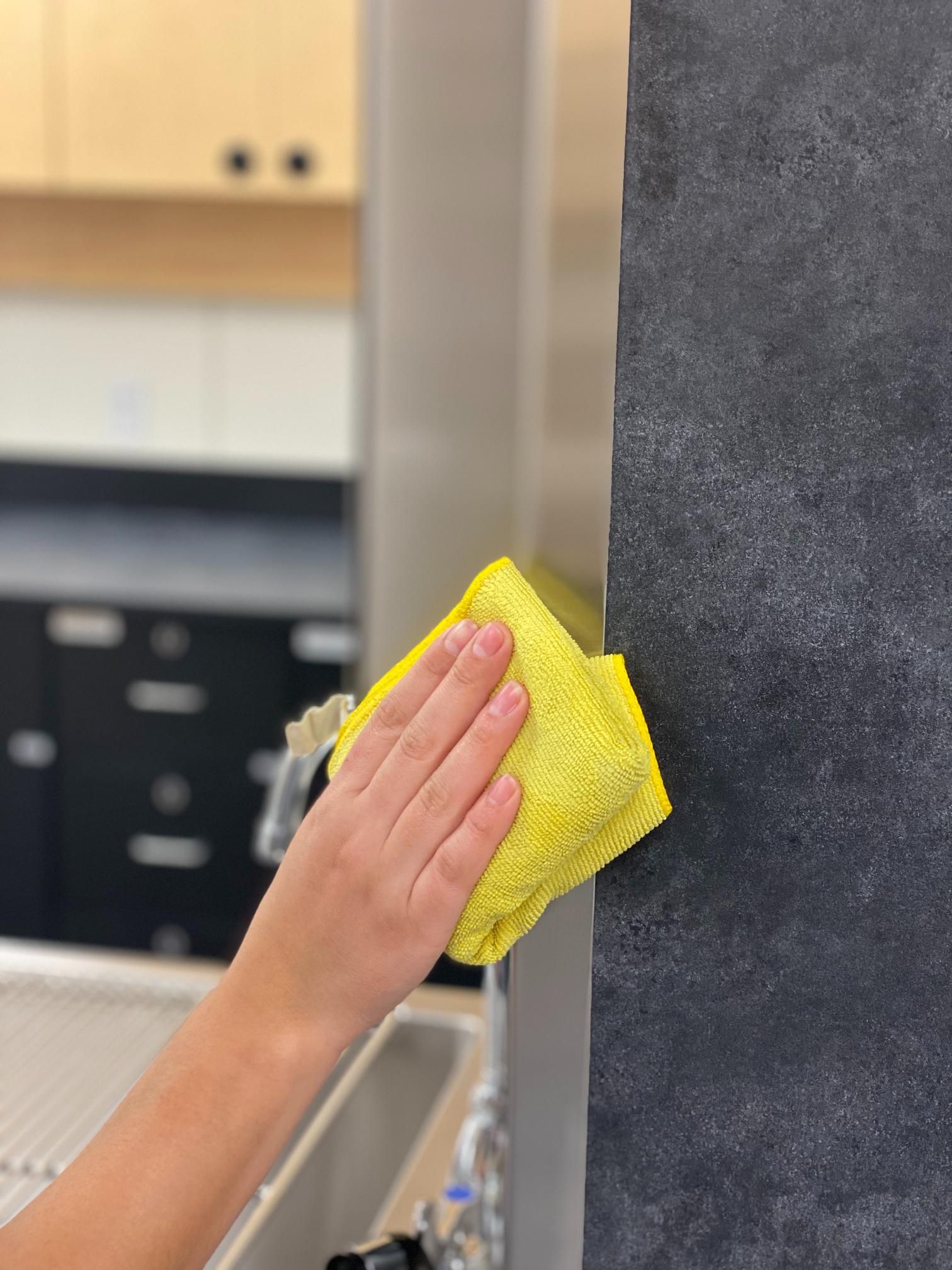 A person is cleaning a wall with a yellow towel in a kitchen.