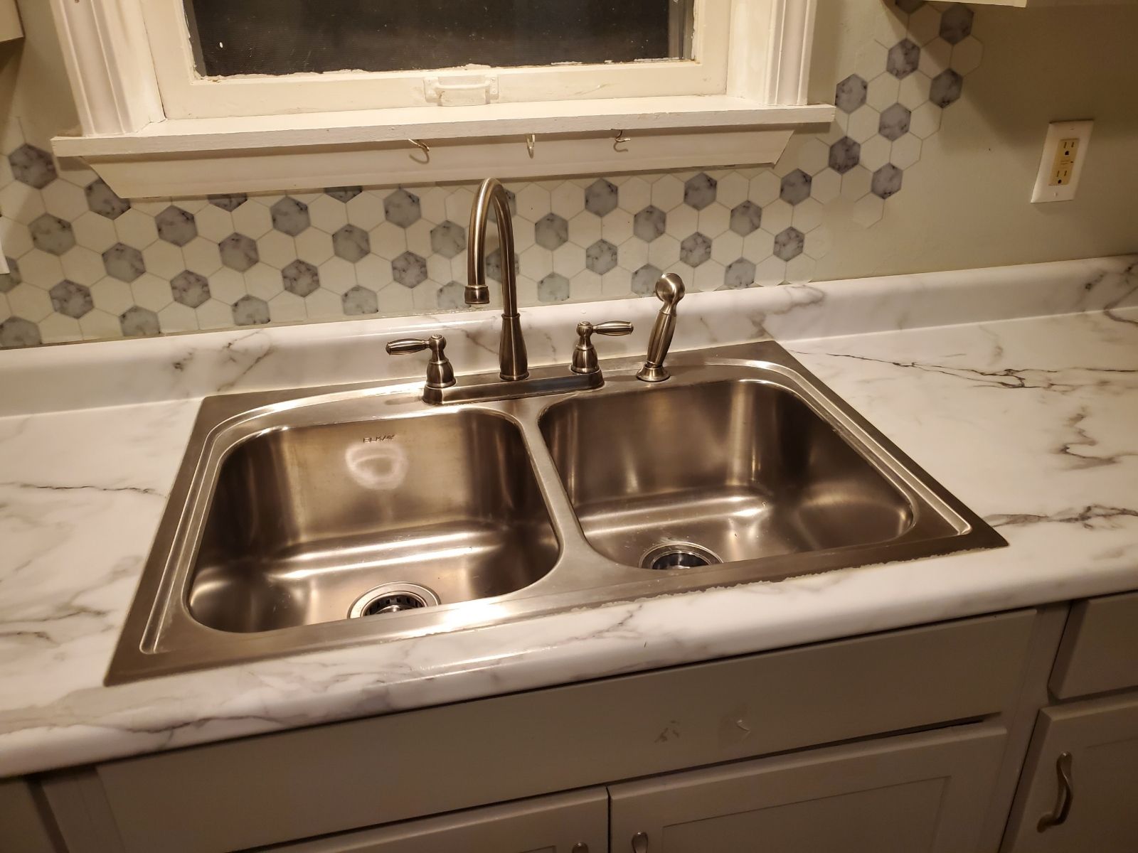 A stainless steel kitchen sink is on a marble counter top.
