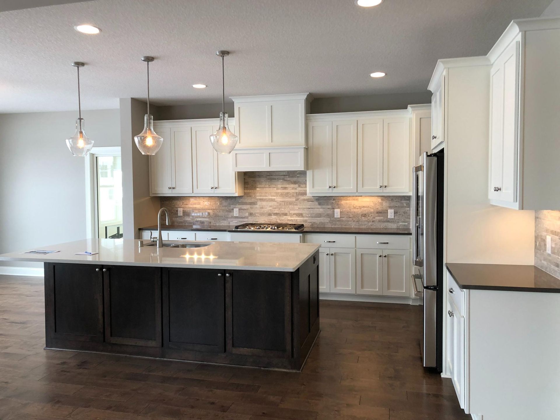 Modern kitchen with white cabinets, dark island, and stainless steel appliances.