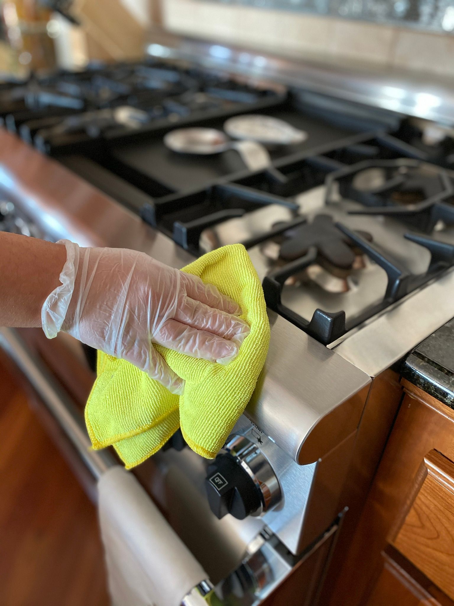 A person wearing gloves is cleaning a stove with a yellow cloth.