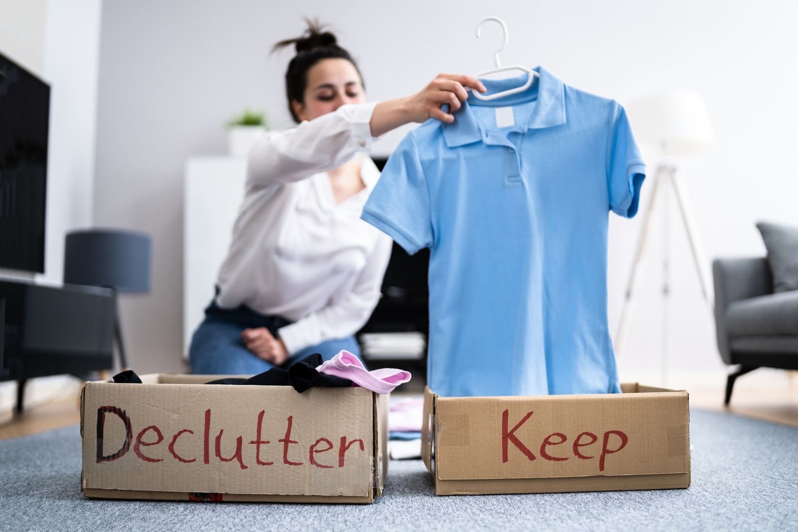 A woman is putting a blue shirt in a cardboard box.
