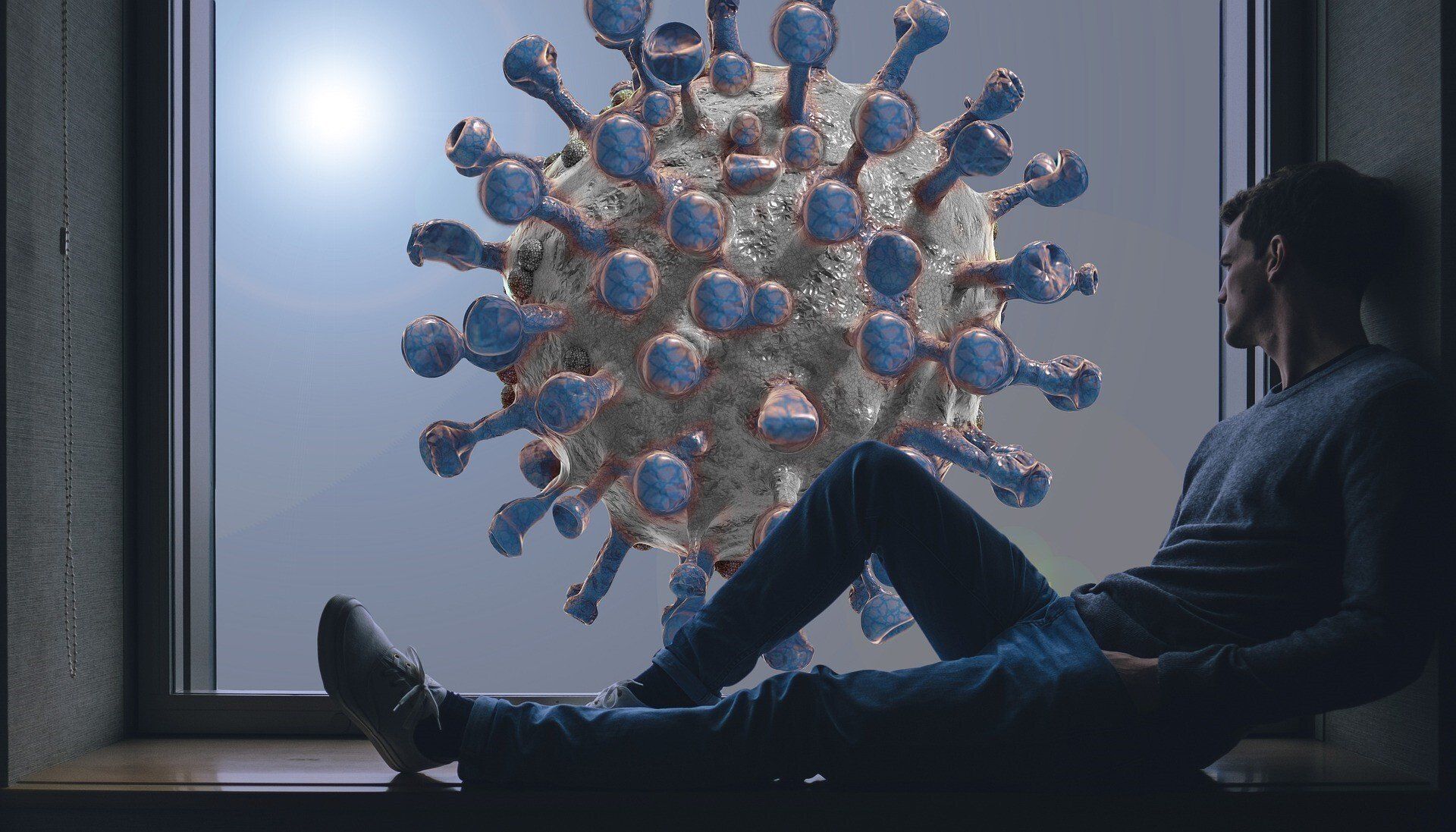 A man is sitting in front of a window with a virus behind him.