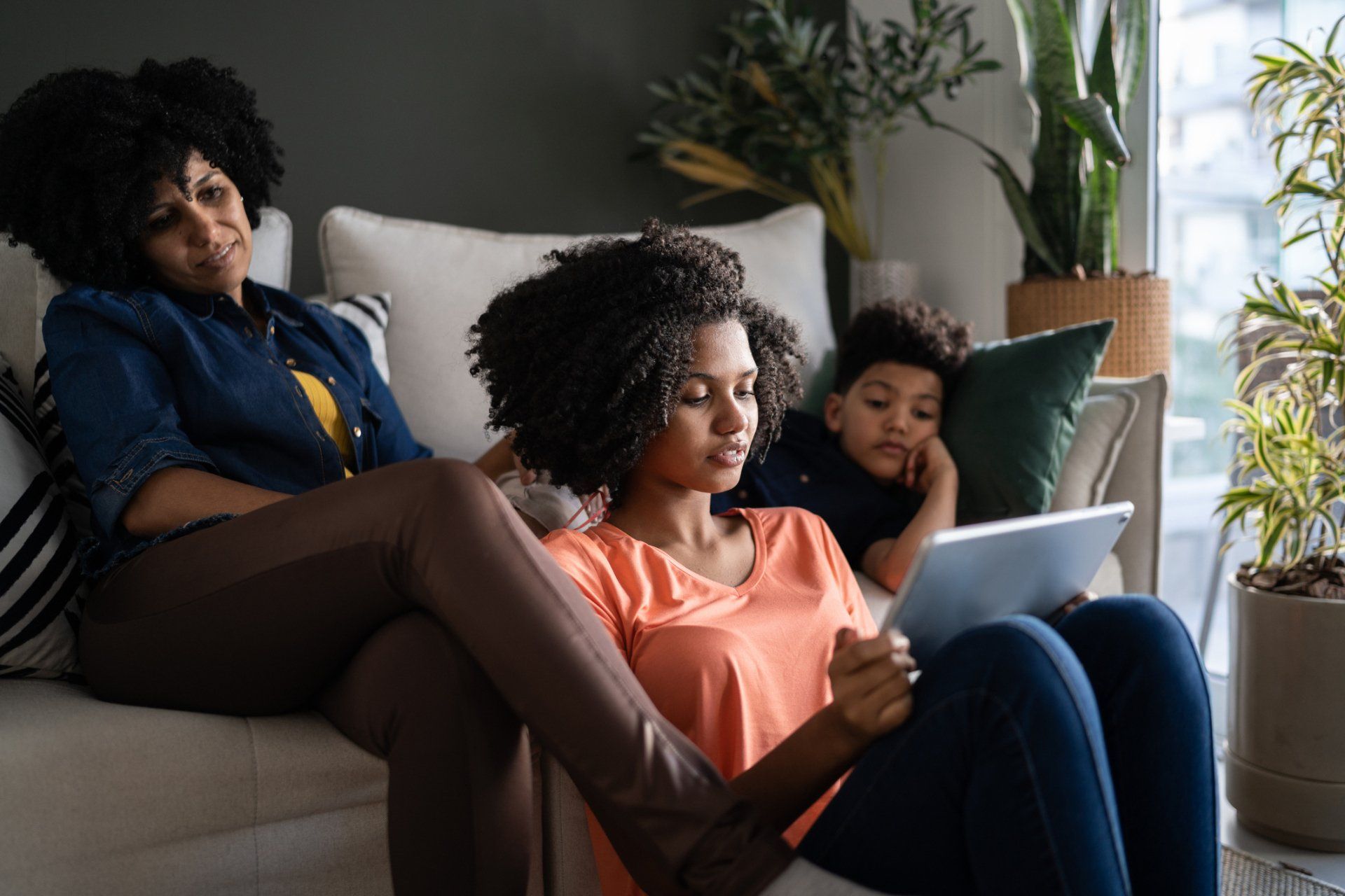 A woman and a child are sitting on a couch looking at a tablet.