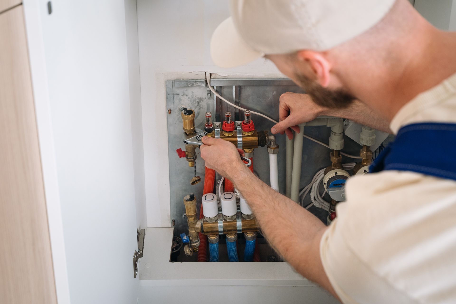 A plumber is working on a heating system in a cabinet.