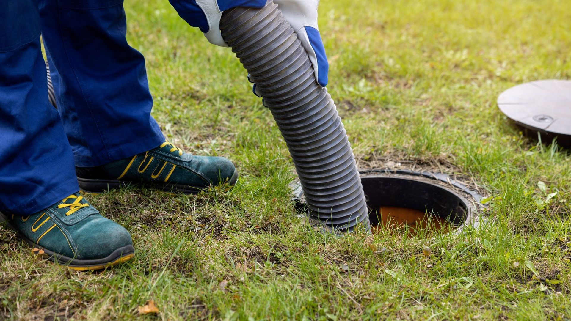 A man is pumping sewage into a manhole cover with a vacuum hose.