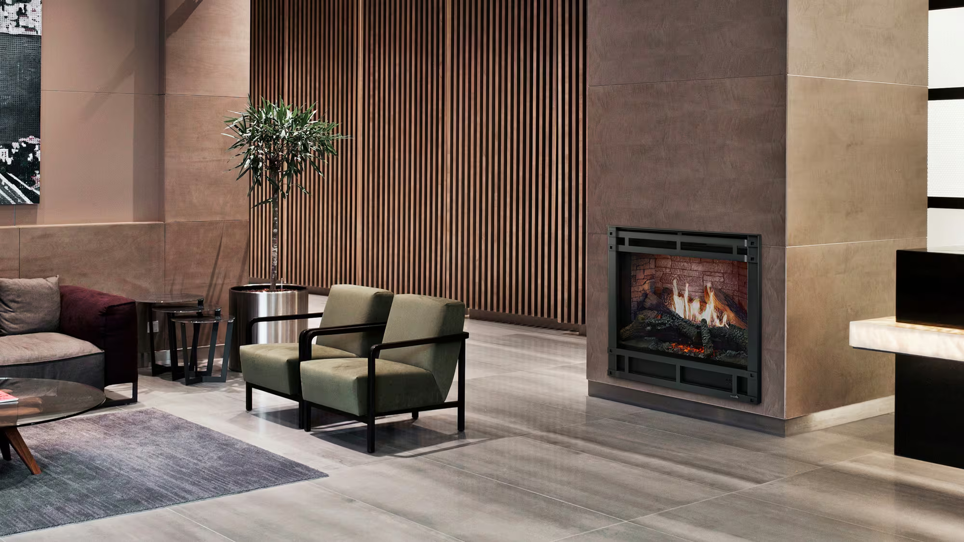 Lounge area with fireplace, chairs, and a tree. Earthy tones: brown, green, and gray. Modern design.